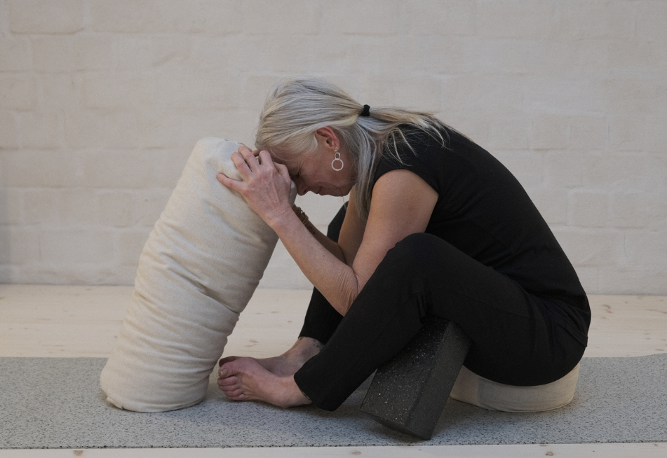 Frau mit Kopf auf Bolster, mit Block auf Meditationskissen und Yogamatte