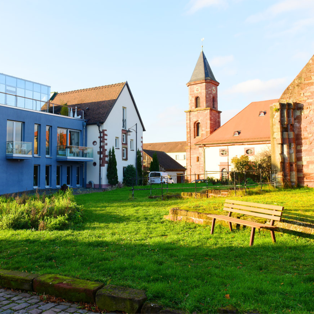 Lichtdurchflutete Wiese vor einem Alt- und Neubau