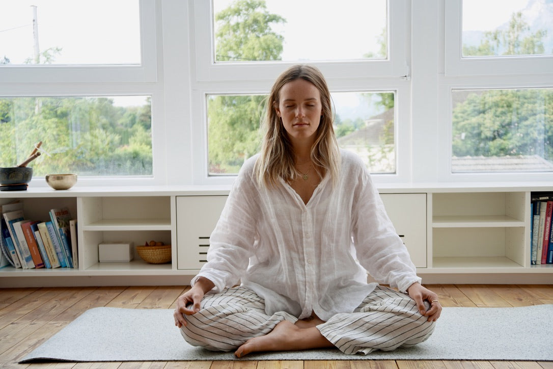 yoga teacher alexa has her eyes closed and sits on her yoga mat