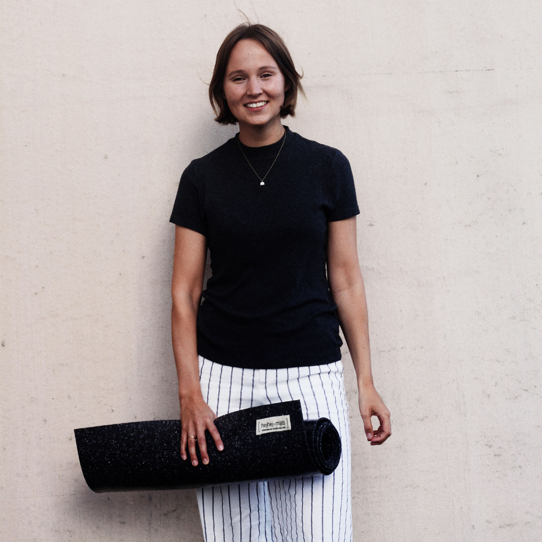 Anna mit schwarzem T-Shirt und der dunklen hejhej-mat in der Hand mit kurzen Haaren und einem Lächeln