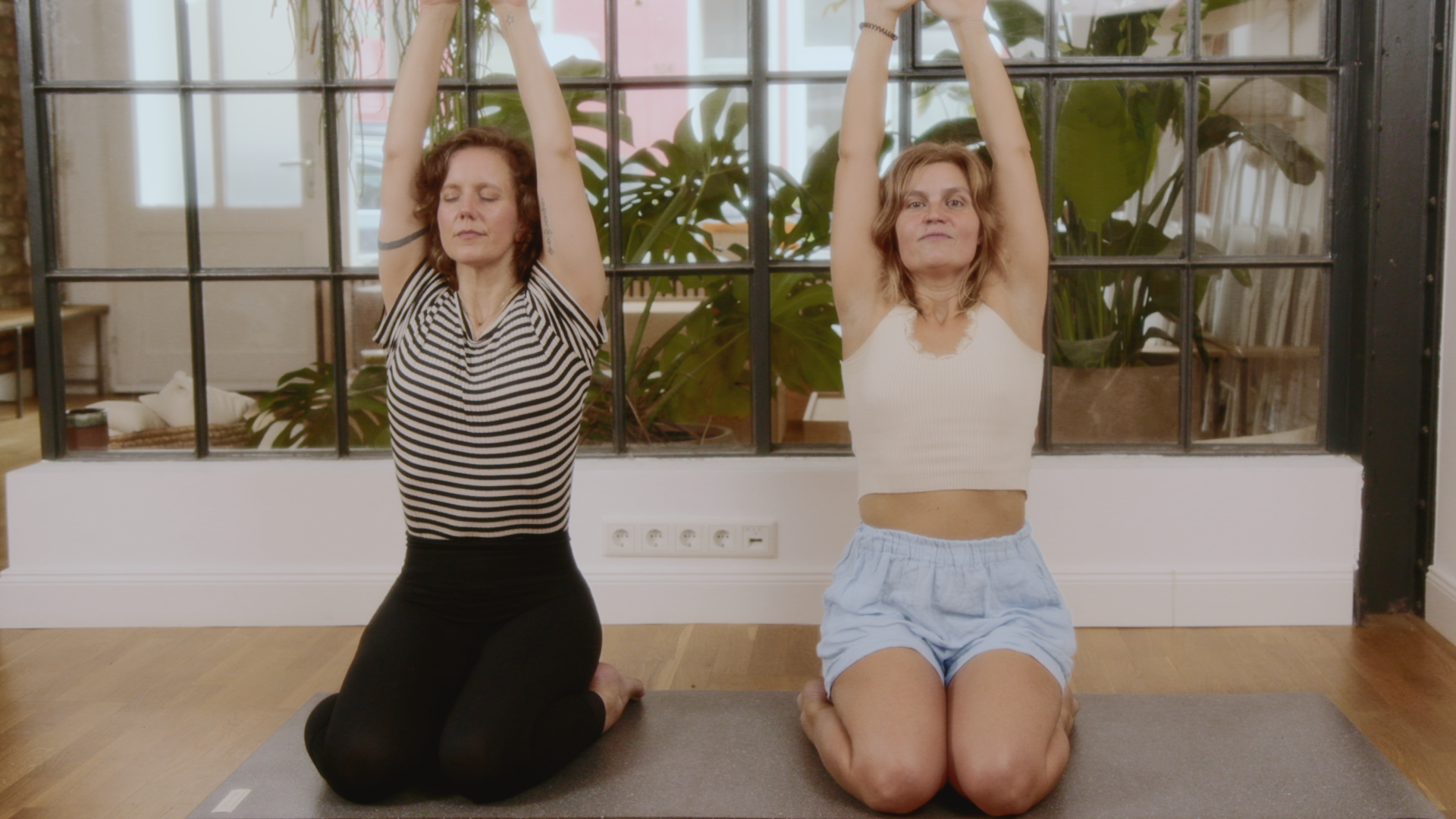 Zwei Frauen machen eine Katonah Atmen Übung und halten ihre Arme in die Luft