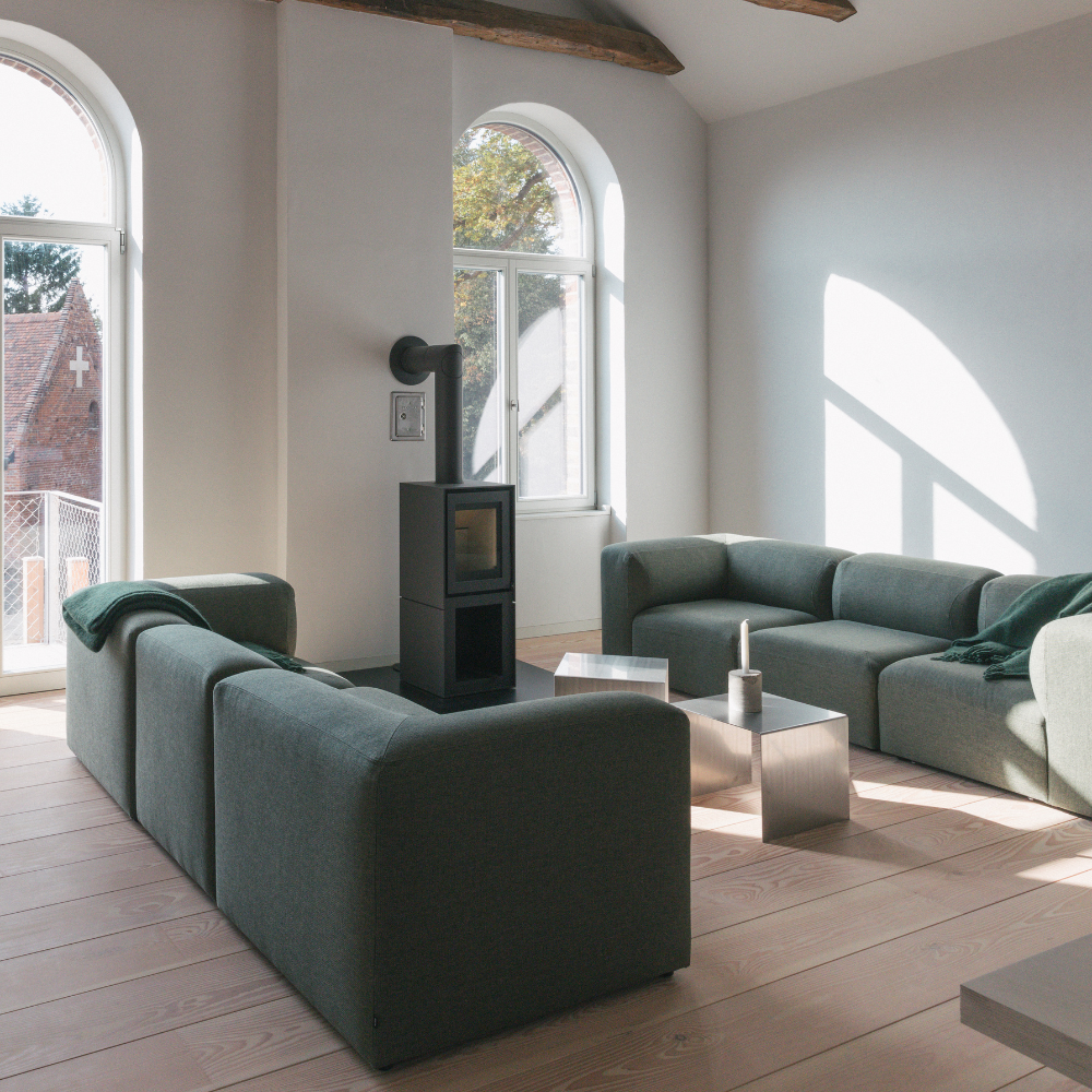 Wohnzimmer im Verwalterinnenhaus mit Kamin, großen Fenstern und grünen Sofas