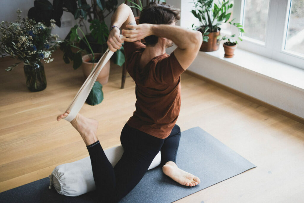 Man practicing the yoga asana pigeon pose and uses the hejhej-strap to deepen his posture