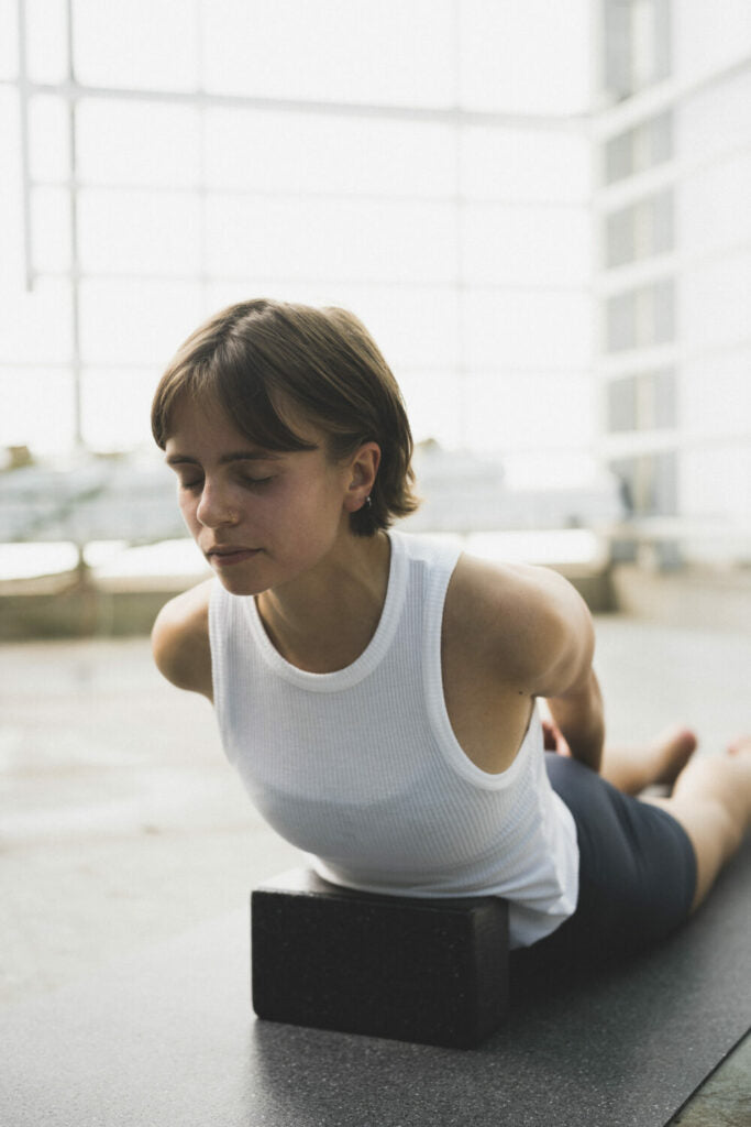 Woman with short hair lies with her chest on the sustainable yoga block by hejhej-mats