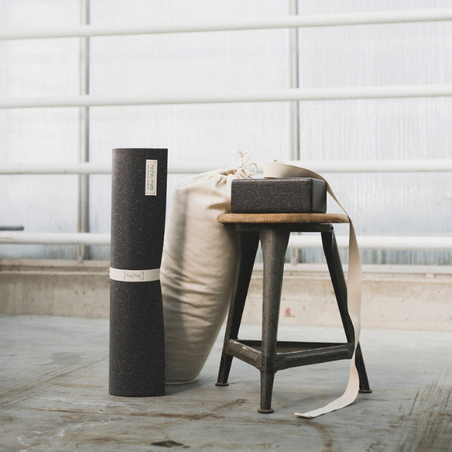Um einen Hocker herum stehen die eher dunkle hejhej-mat und der hejhej-bolster. Der Yogablock und der Yogastrap liegen auf dem Hocker. Perfekt für die Yogapraxis zuhause.