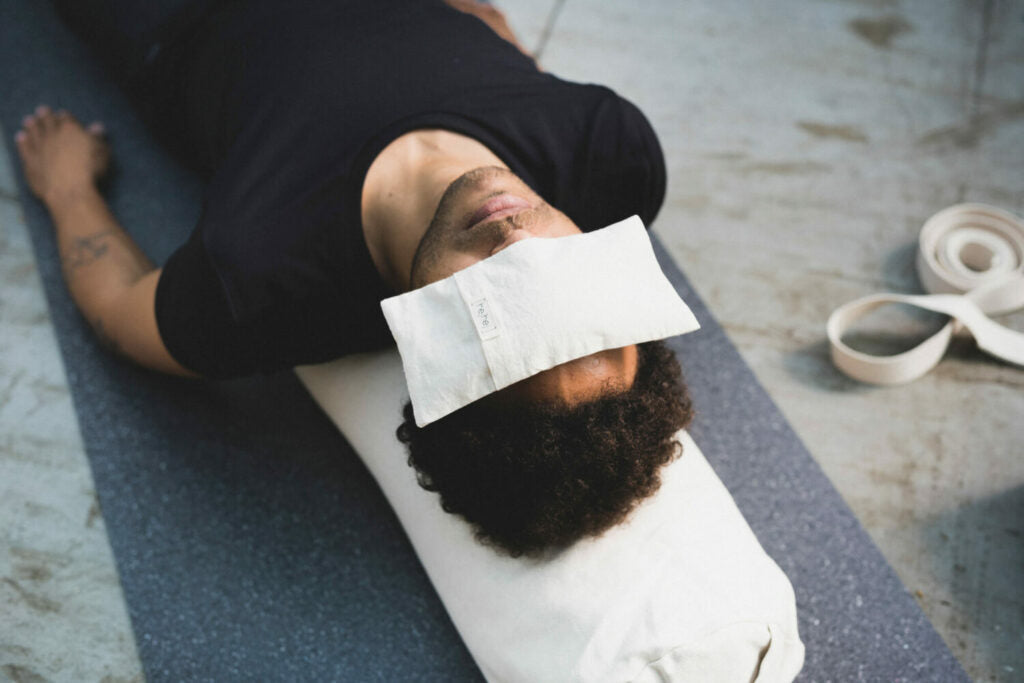 The sustainable eye pillow lies on the face of a person lying in Savasana.