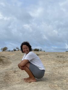 A woman sits on the ground and wraps her arms around her legs