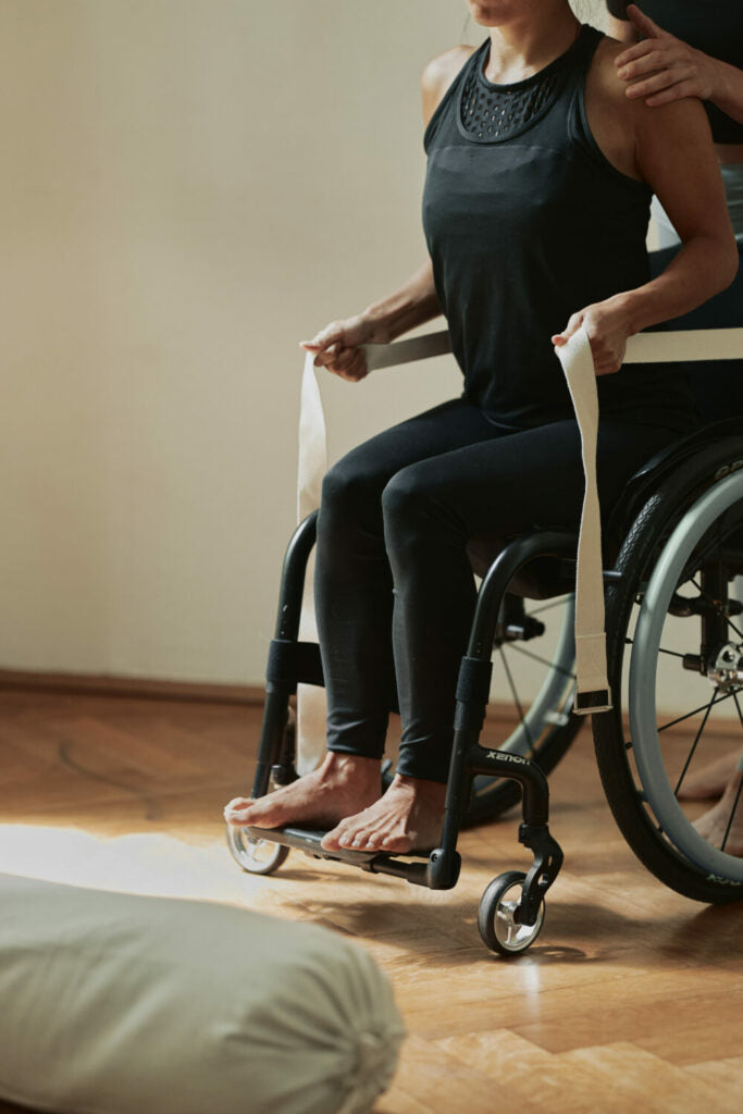 A woman sits in a wheelchair and stretches her back with the hejhej-strap